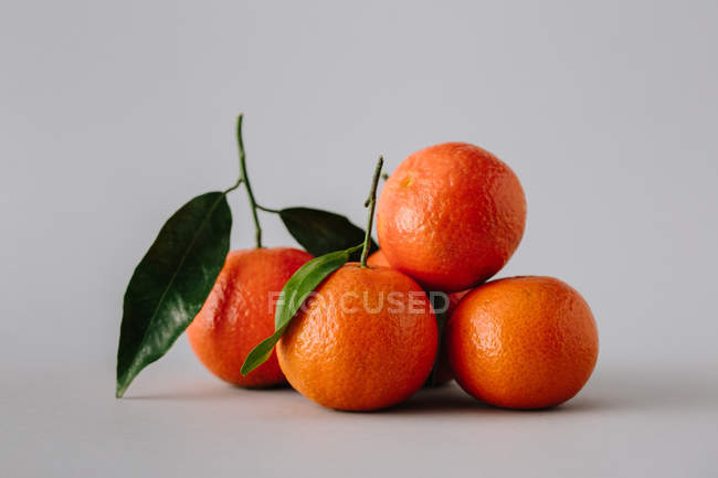 Pile of fresh ripe unpeeled tangerines with green leaves on gray background — Stock Photo