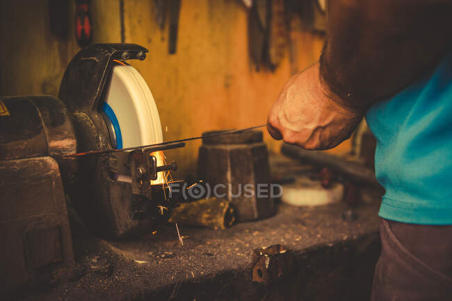 Recadrage forgeron à l'aide de meule pour affûter la lame en métal dans l'atelier professionnel — Photo de stock