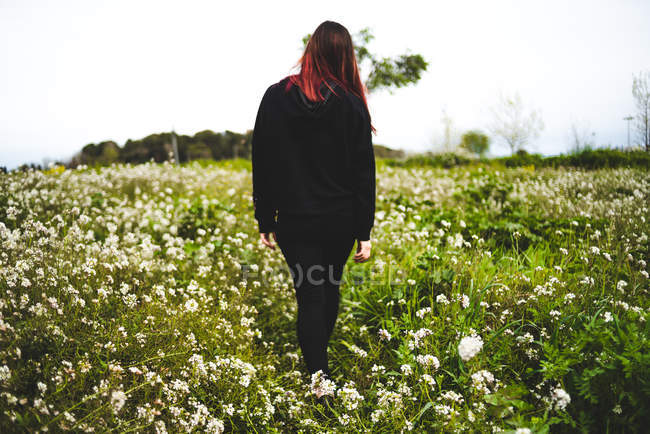 Jovem mulher vestindo preto de pé no gramado com flores amarelas — Fotografia de Stock