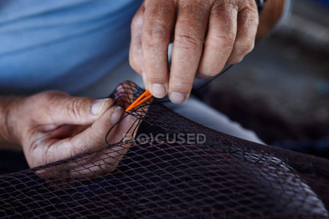 Cultures de dessus vue de l'homme tenant le filet de pêche dans les mains et coupant au couteau — Photo de stock