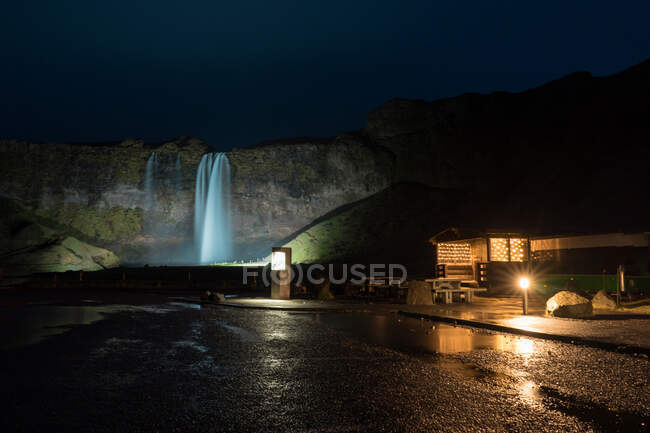Bau eines winzigen Hotels in der Nähe eines fantastischen Wasserfalls in der Nacht in Island — Stockfoto