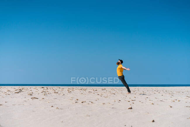 Seitenansicht eines bärtigen Mannes, der am Strand am Meer in den Sand fällt. — Stockfoto