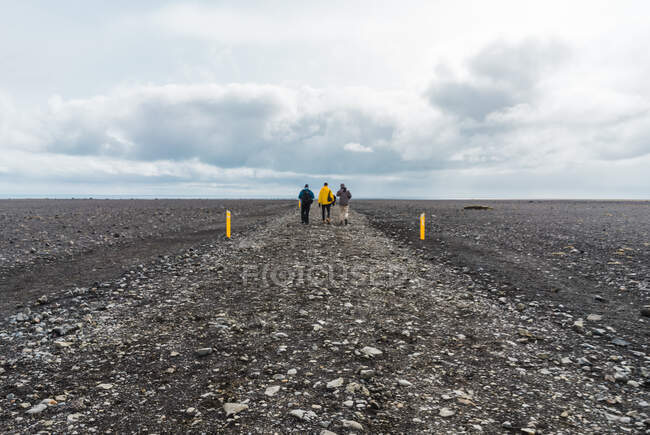 Vista posteriore di turisti lontani che camminano lungo una bella strada di ghiaia che attraversa la campagna pietrosa in Islanda — Foto stock