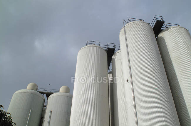 De baixo da visão de tanques brancos de alto cilindro colocados do lado de fora no fundo do céu nublado sombrio — Fotografia de Stock