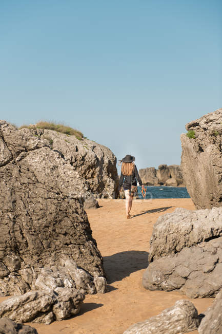 Женщина в элегантном наряде прогуливается по песчаному берегу посреди валунов в море — стоковое фото