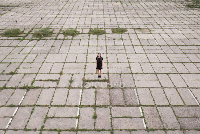 Vue à distance de la femme en robe noire debout sur un pavé de béton spacieux avec de l'herbe verte — Photo de stock