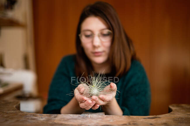 Donna in camicetta verde e occhiali seduti al tavolo da lavoro in officina e mostrando decorazione lanuginosa — Foto stock