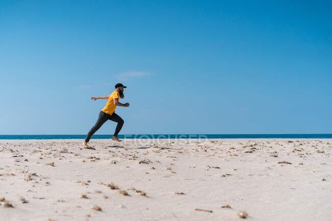 Vue latérale de l'homme barbu tombant sur le sable sur la plage à l'océan. — Photo de stock