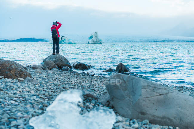 Back view of male in warm clothes and backpack taking picture of scenic lake in Skaftafell, Iceland and Vatnajokull — Foto stock