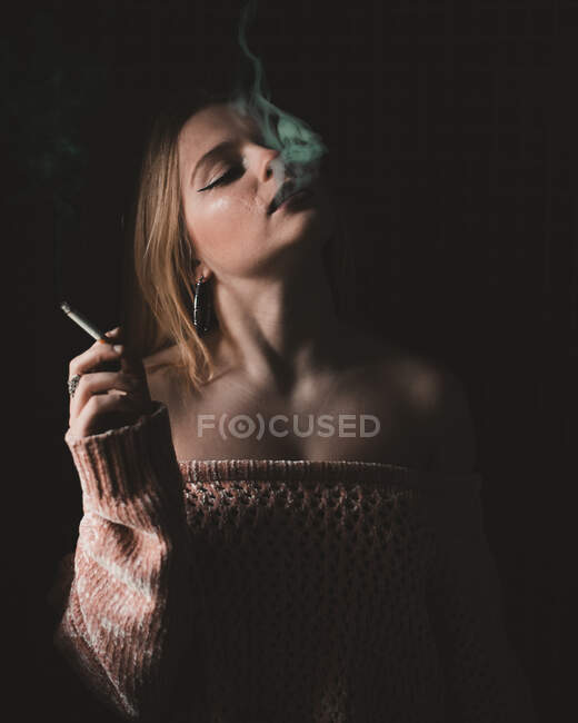 Attraktive junge sinnliche Frau raucht Zigarette auf dunklem Hintergrund. — Stockfoto