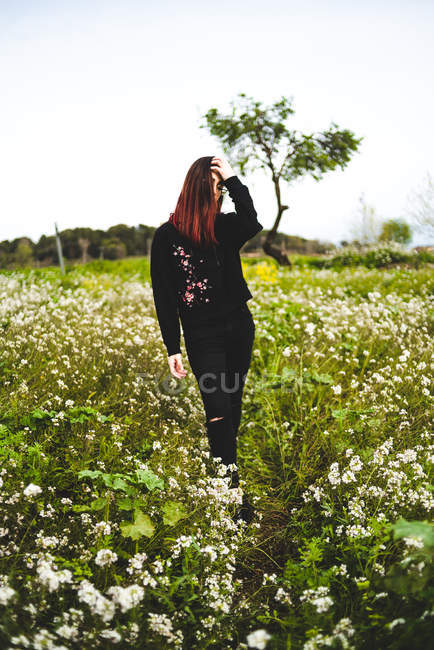 Young woman wearing black standing on lawn with yellow flowers — Stock Photo