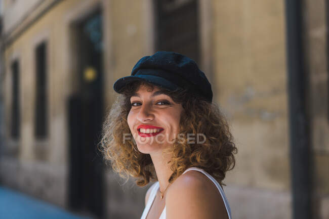Hübsche lockige Frau mit schwarzer Mütze, kurzer Hose und Tank-Top, die auf der Straße in die Kamera schaut — Stockfoto