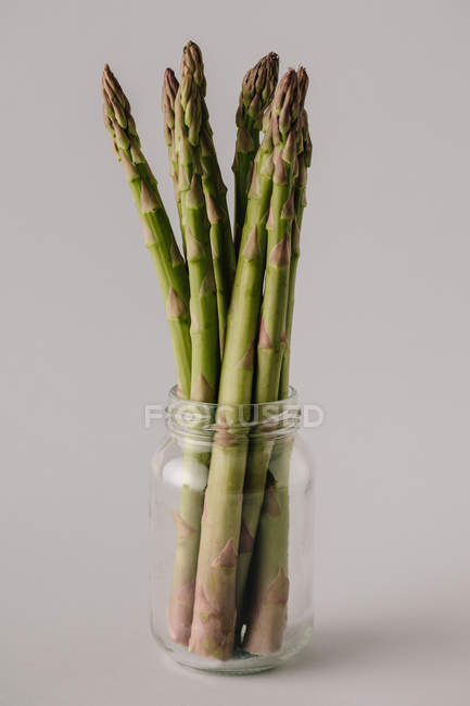 Bocal en verre avec tiges d'asperges mûres non cuites sur fond gris — Photo de stock