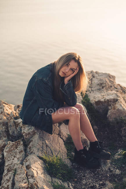 Giovane signora seduta su pietre guardando la fotocamera — Foto stock