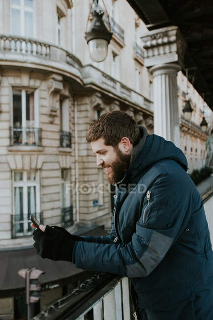Вид сбоку взрослого мужчины, стоящего со смартфоном у поручня на улице в Париже, Франция. — стоковое фото