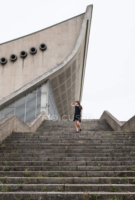 Von unten Aufnahme einer Frau in schwarzem Kleid, die eine graue Betontreppe hinuntergeht, mit modernem Gebäude im Hintergrund — Stockfoto