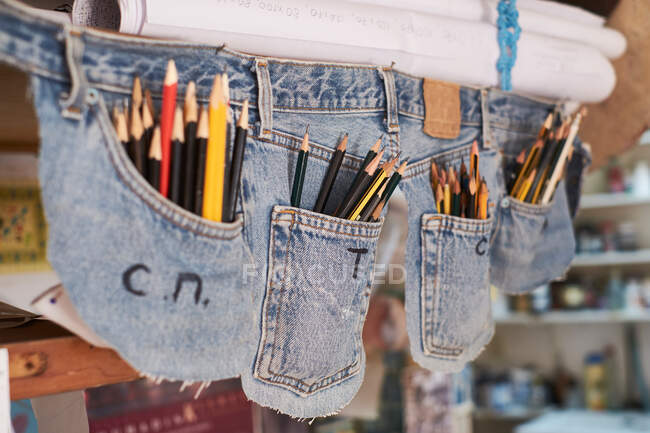 Funda creativa hecha de bolsillos vaqueros llenos de lápices de escritura colgando en la habitación - foto de stock