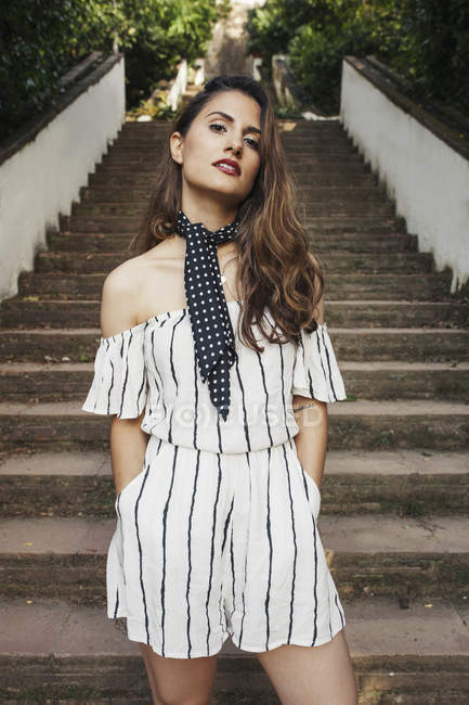 Portrait de femme élégante en combinaison rayée debout sur les escaliers dans le parc — Photo de stock