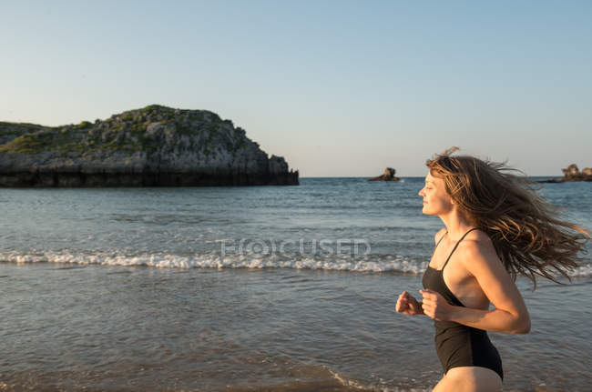Jovem mulher em maiô correndo perto do mar — Fotografia de Stock