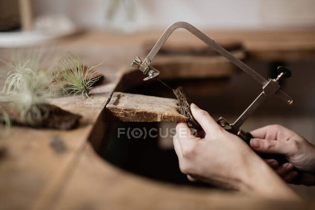 Cultiver gros plan mains de la personne sculpture décoration de morceau d'écorce d'arbre avec instrument sur ? desk — Photo de stock