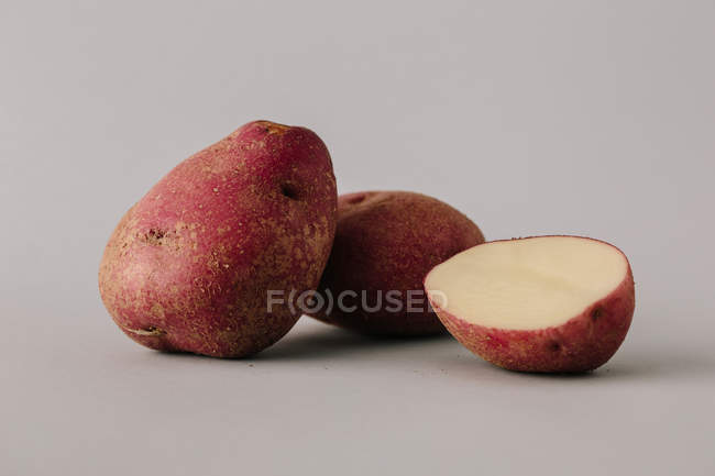 Свіжа ціла і наполовину картопля на сірому фоні — стокове фото