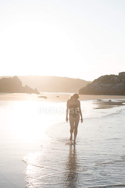 Unrecognizable woman walking on sand near sea in sunlight — Stock Photo