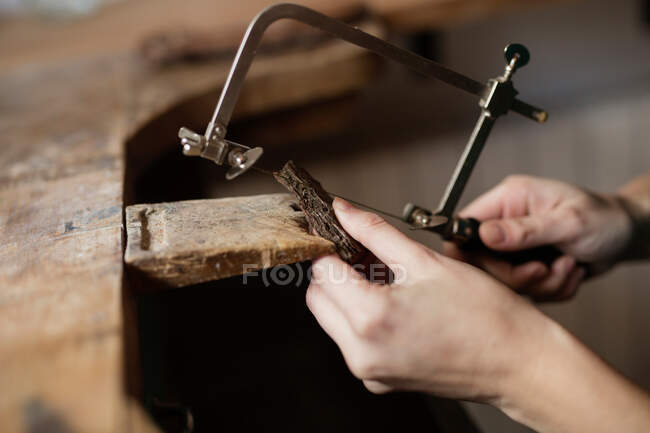 Руки крупным планом человека, вырезающего украшение куска коры дерева с инструментом на столе? — стоковое фото