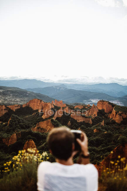 Visão traseira do fotógrafo embaçado com câmera fazendo foto de pé em cima de colinas no fundo da paisagem na Cantábria, Espanha — Fotografia de Stock