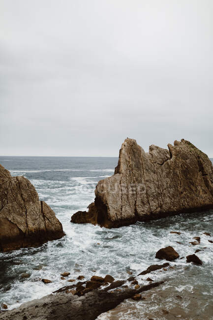 Pedras em mar ondulado? sob céu cinza nublado em Cantabria, Espanha — Fotografia de Stock