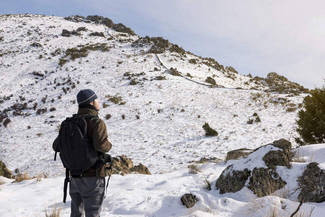 Joven con una mochila de senderismo disfrutando en las montañas nevadas en un día soleado de invierno. - foto de stock