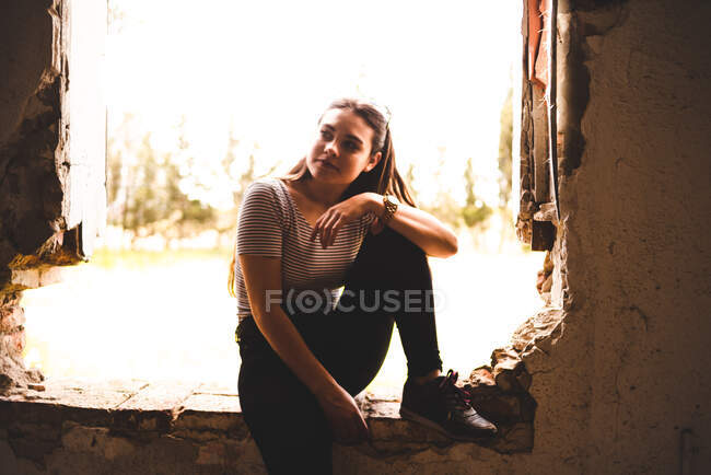 Charming young woman admiring nature sitting in breach in wall of abandoned building — Stock Photo