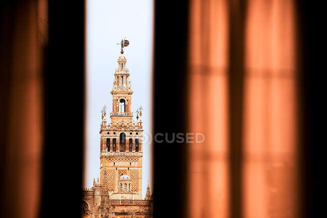 Hoher alter Turm durch halb geöffnetes Fenster mit Vorhängen bedeckt — Stockfoto