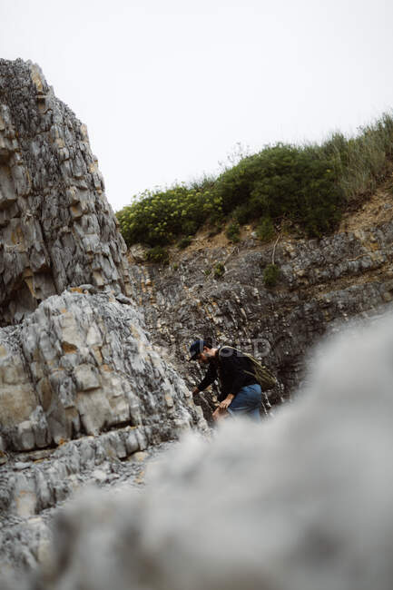Maschio che cerca di arrampicarsi su roccia in berretto con zaino in Cantabria, Spagna — Foto stock