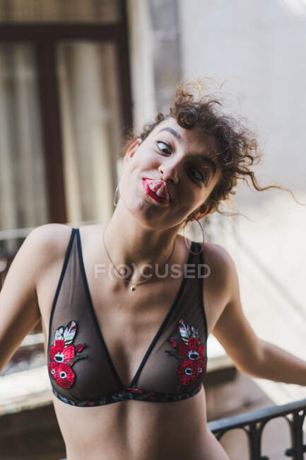 Entzückendes junges Mädchen in Spitzenunterwäsche, die Fratze macht und die Nase mit der Zunge berührt und Spaß auf dem Balkon hat — Stockfoto