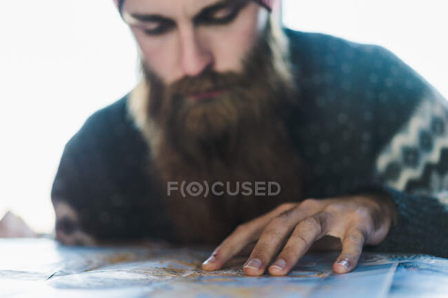 Crop view of bearded male in hat searching place on map of Iceland — Stock Photo