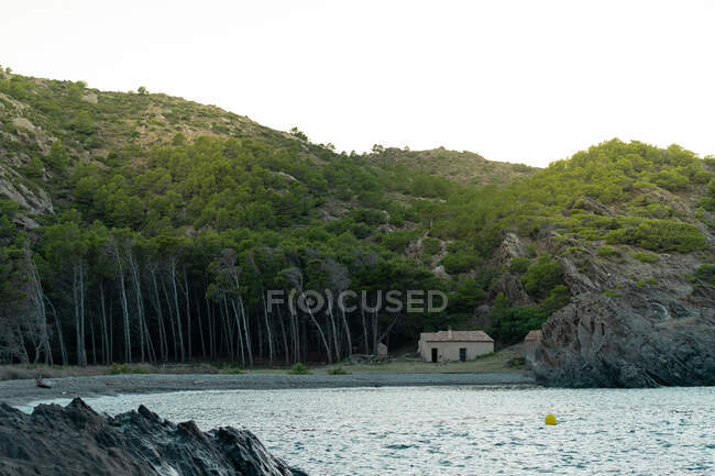 Pequeña choza de pie cerca de la montaña y el bosque en la hermosa costa en Tavallera - foto de stock