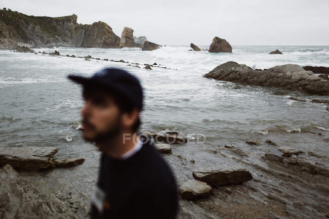 Maschio sfocato in piedi sul mare pietroso e guardando altrove in Cantabria, Spagna — Foto stock