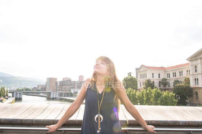 Jovem mulher desfrutando sol brilhante enquanto se inclina na cerca — Fotografia de Stock