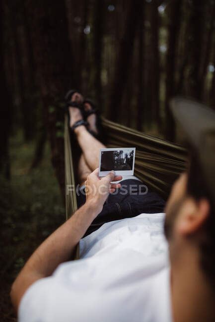 Back view of man lying in hammock in forest and looking at photo in Cantabria, Spain — Stock Photo