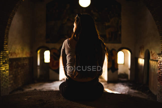 Gesichtslose junge Frau sitzt auf einem Felsvorsprung, während sie Zeit in alten, verfallenen Gebäuden verbringt — Stockfoto