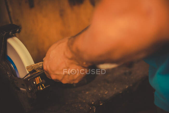 Crop smith using grindstone to sharpen metal blade in professional workshop — Stock Photo