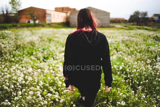 Jovem mulher vestindo preto de pé no gramado com flores amarelas — Fotografia de Stock