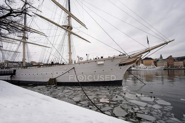 Beautiful sail vessel standing in port of nice Nordic town during spring ice drift. — Stock Photo