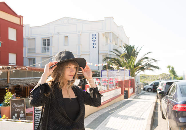 Young woman in elegant hat walking on street of resort town — Stock Photo