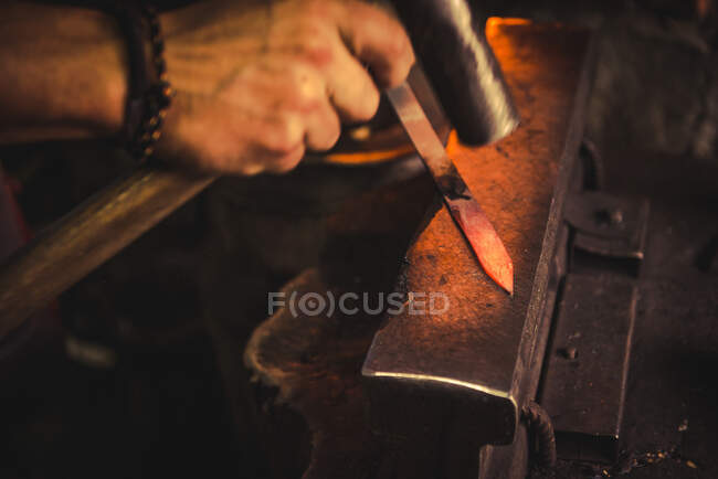 Uomo anonimo che utilizza hummer per forgiare lama da pezzo di metallo in officina professionale — Foto stock