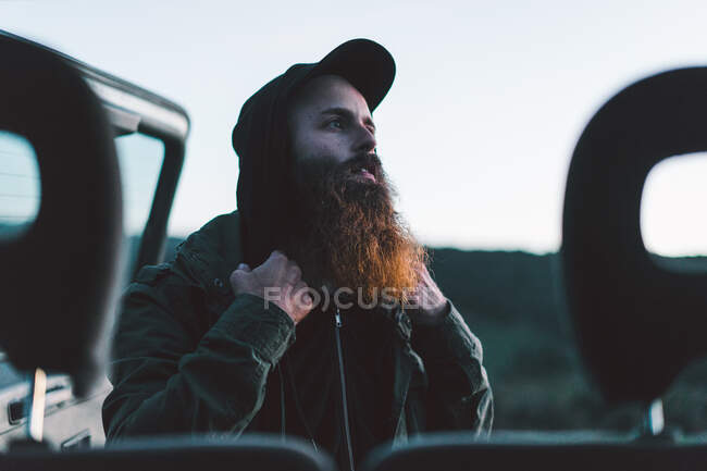 Vista laterale dell'uomo barbuto adulto che apre il bagagliaio dell'auto e distoglie lo sguardo nella natura. — Foto stock