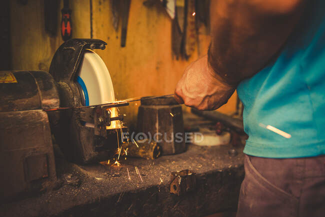 Recadrage forgeron à l'aide de meule pour affûter la lame en métal dans l'atelier professionnel — Photo de stock