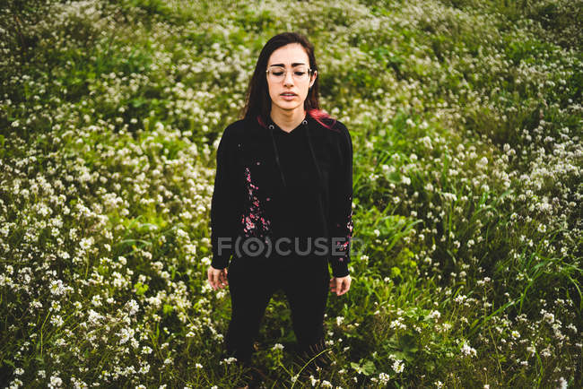Стильная молодая женщина с закрытыми глазами, стоящая в зеленом поле с белыми цветами — стоковое фото