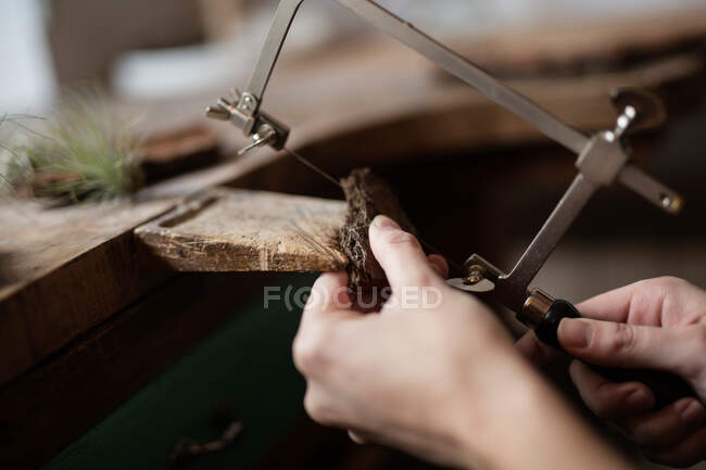 Cosecha de cerca las manos de la persona tallado decoración de la pieza de corteza de árbol con el instrumento en? desk - foto de stock