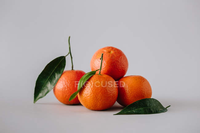 Pile de mandarines fraîches mûres non pelées avec des feuilles vertes sur fond gris — Photo de stock